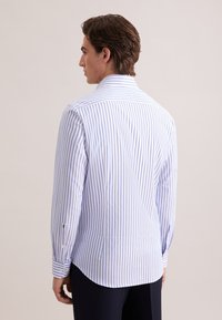 Camicia da uomo a maniche lunghe con righe verticali bianche e azzurre, caratterizzata da un colletto a punta, polsini con bottoni e orlo curvo.