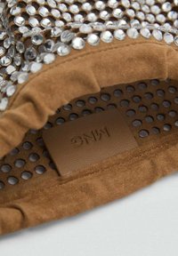 Smešasti smešasti smešasti u smeštraj dožnini sa mrežastim dizajnom ukrašenim prozirnim rhinestones. Uključuje teksturiranu oznaku loga unutar.
