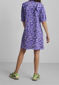 Purple floral dress with short sleeves, ruffle accents on shoulders, and a loose fit. Paired with chunky sneakers with green accents.