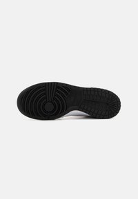 Semelle en caoutchouc noir avec des motifs de bande de roulement circulaires et linéaires ; présente le logo Nike. Partie supérieure lisse en blanc pour le contraste.