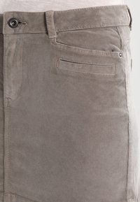 Nahaufnahme von hellbraunen Cordhosen mit Knopf, Gürtelschlaufe und Seitentaschen-Details.