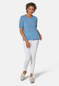 Hellblaues Pullover mit Puffärmeln und rundem Ausschnitt, kombiniert mit weißen Skinny-Jeans und beigen Sneakers. Glatte Textur, lässiges Design.