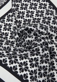Sort og hvidt stof med et blomsterdesign, der har symmetriske blomster og trekantede accenter, lavet af glat, let materiale.