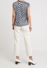 Blusa de manga corta con patrón de diamantes en azul marino y blanco, combinada con pantalones cortos en blanco roto y zapatos de tacón cuadrado blancos.