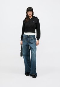 Melns crop tops ar kapuci, zilas plaša piegriezuma džinsu bikses un melna rokassoma. Gluda kokvilnas auduma; priekšējās kabatas biksēs; minimālistisks dizains.