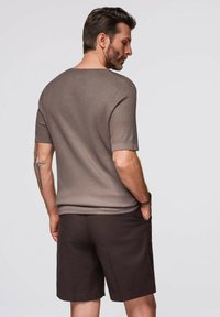 Maglietta a maniche corte marrone a costine con scollatura rotonda, abbinata a pantaloni corti marroni scuri. La vista posteriore mostra un fit rilassato e semplicità.