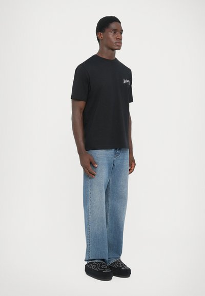 Schwarzes Baumwoll-T-Shirt mit Rundhalsausschnitt, kurzen Ärmeln und weißem "Iceberg"-Logo auf der linken Brust; kombiniert mit hellblauen geraden Jeans.