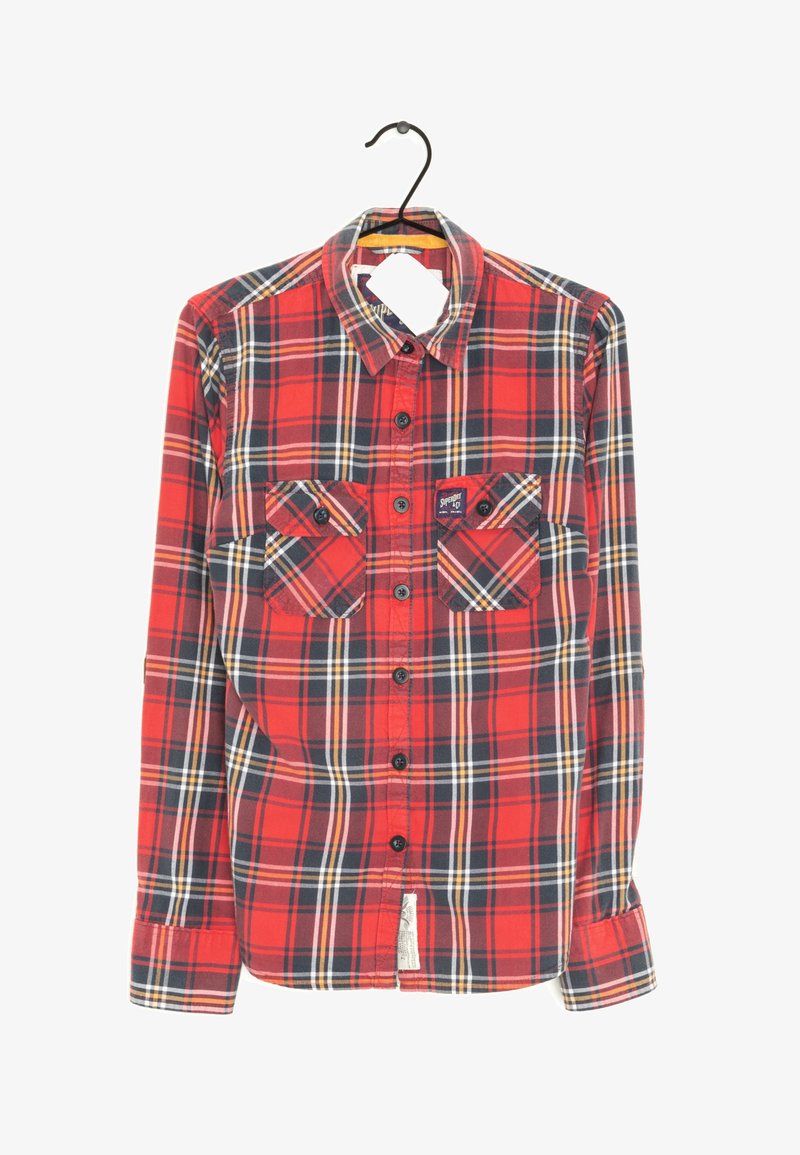 Chemise à manches longues à carreaux rouges et noirs, boutonnée, avec deux poches poitrine devant, suspendue sur un cintre noir contre un fond blanc.