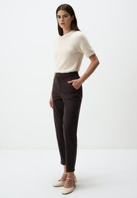 Beige, korte mouwen, fuzzy trui met een gestructureerde halslijn, gedragen met hoge, donkerbruine broeken en lichte, stevige hakken.