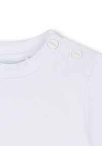 T-shirt en coton blanc avec un col rond, présentant deux boutons-pression blancs avec le logo "BOSS" sur l'épaule. Texture lisse, design décontracté.