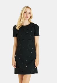 Vestido negro de manga corta con escote redondo y adornos plateados dispersos. La tela tiene una textura suave y un diseño ajustado.