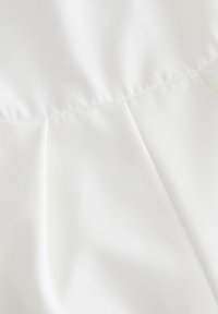 Gros plan d'un tissu blanc avec une texture lisse et des coutures pliées subtiles formant des formes géométriques.