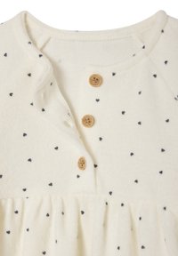 Helles Kleid aus Strukturstoff mit schwarzen Herzmustern, fünf Holzknöpfen und gerafftem Taillenbereich.