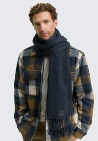 Marineblauer Schal aus weichem Stoff mit ausgefransten Rändern. Locker getragen zu einer karierten Jacke in Blau, Braun und Cremetönen.