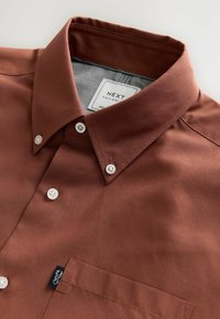 Rostbraunes Hemd mit Knöpfen, weißen Knöpfen, einer Brusttasche und einem sichtbaren NEXT-Label für die Maße im Kragen.
