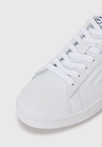 Adidași albi cu un superior din piele netedă, vârf rotund și șireturi albe. Prezintă cusături minime și o talpă din cauciuc alb texturată.
