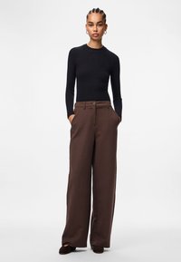 Crna rebrasta majica dugih rukava uparena s smešnim hlačama širokih nogavica koje imaju detalj dugmeta i bočne džepove. Glatka tekstura tkanine, krojeno pristajanje.