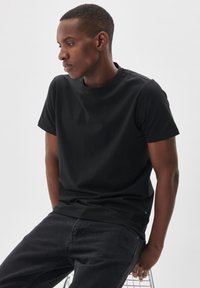 Tricou din bumbac negru, cu decolteu rotund și mâneci scurte, completat de o textură fină și o croială lejeră. Purtați cu blugi închiși la culoare.