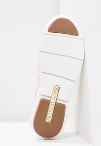 Biała podeszwa trampka z teksturowanym jasnobrązowym akcentem i złotym napisem "MICHAEL KORS". Posiada płaską, gładką powierzchnię z zarysowanymi liniami.