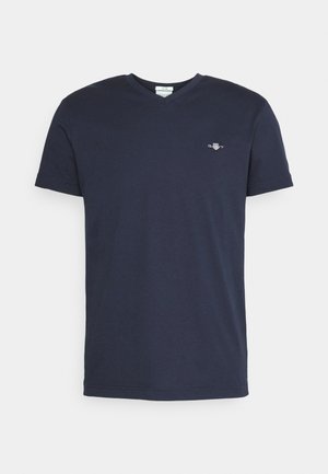 Camiseta de algodón de color azul marino con cuello en V y mangas cortas, que presenta un pequeño logo bordado en el lado izquierdo del pecho. Textura suave.