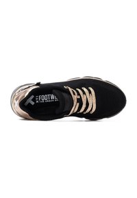Zapatilla negra con parte superior de malla, cordones metálico dorado y un talón dorado brillante en contraste. Cuenta con una suela acolchada y detalle de logo.