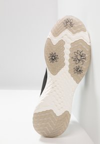 Černá podrážka tenisky s texturovanou bílou a béžovou gumou, zdobená květinovými vzory. Hladký povrch s cikcak a tečkovanými vzory.