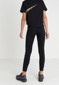 T-shirt nero tagliato con il logo Nike a stampa leopardata; abbinato a leggings neri con un accento a stampa leopardata; scarpe da ginnastica nere.