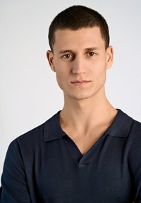 Mörkblå polo tee med V-hals; slät, fint stickad textur. Korta ärmar och en avslappnad passform betonar den diskreta designen.