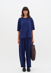 Navy blue oversized t-shirt paired with loose-fitting navy trousers. Model holds a dark brown tote bag; black shoes complete the outfit.