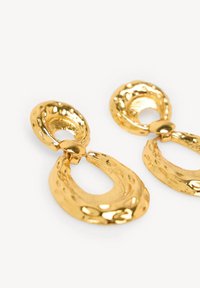 Gouden oorbellen met een geslagen textuur, ovale bovenste schakel en een gebogen, open druppelontwerp voor een hedendaagse uitstraling.