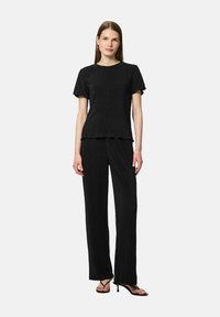 Ensemble noir deux pièces avec un haut à manches courtes texturé et un pantalon à jambe large. Il présente un col rond et un joli volant à l'ourlet du haut.