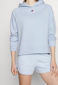 Jasnoniebieska bluza z kapturem z miękkiego materiału, z przednią kieszenią i małym logo. W połączeniu z pasującymi jasnoniebieskimi szortami, oba elementy charakteryzują się luźnym krojem.