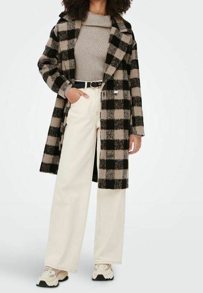 Manteau à carreaux noir et beige au design ajusté, accompagné d'un pull beige côtelé, d'un pantalon large crème et de baskets beiges.