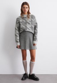 Grijze gesteüpete trui met een geribbelde halslijn, gecombineerd met een grijze uitgerokken rok. Afgewerkt met lichtgrijze kniekousen en zwarte schoenen.