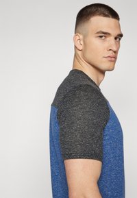 Short-sleeve t-shirt featuring a blue body and charcoal gray sleeves, made of blended fabric with a textured appearance.
