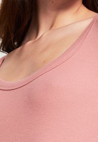 Rosa ribbad linne med vid halsringning och subtil textur som framhäver den figurnära designen. Slät tyg med en mjuk yta.