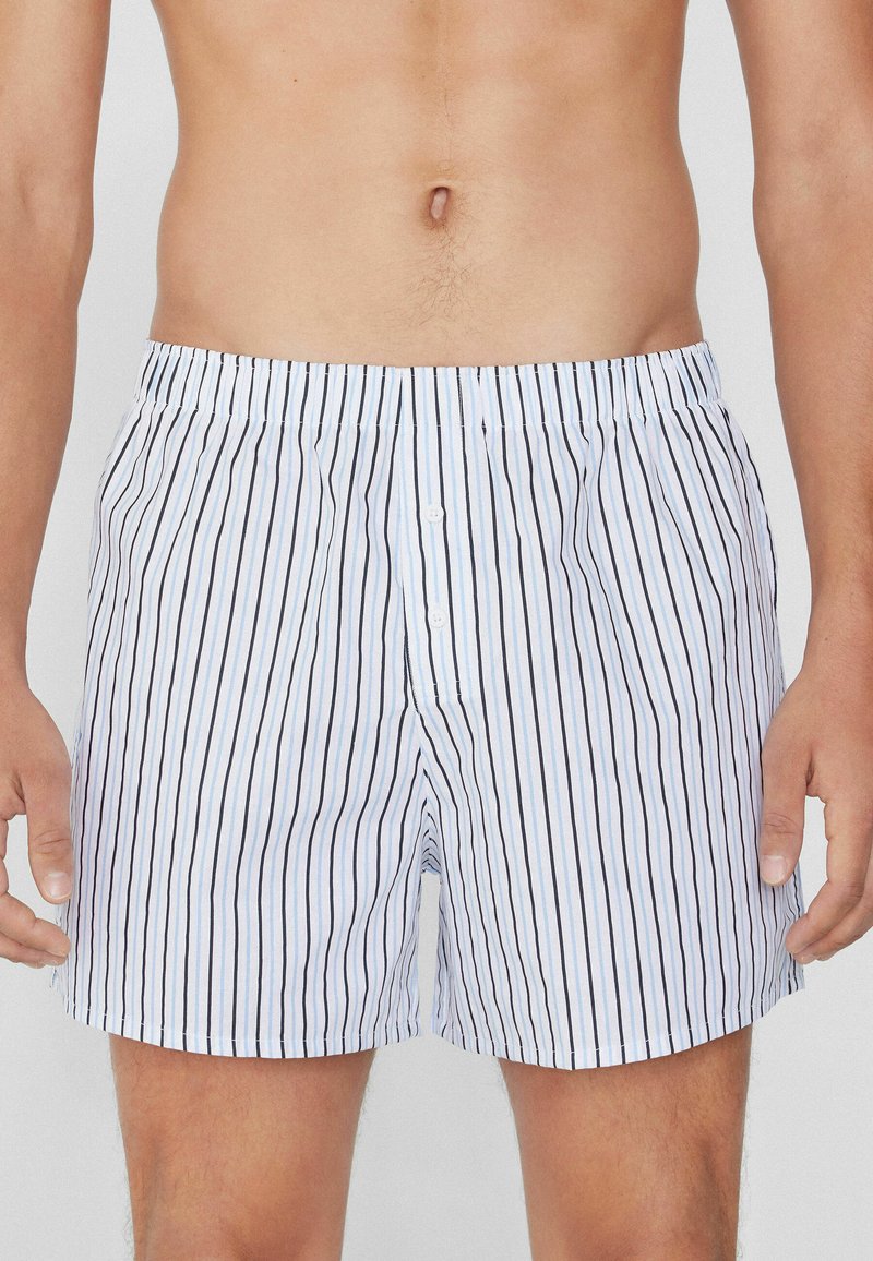 Boxers pour hommes en coton avec des rayures verticales bleues et noires, taille élastique et deux boutons à l'avant pour le maintien.