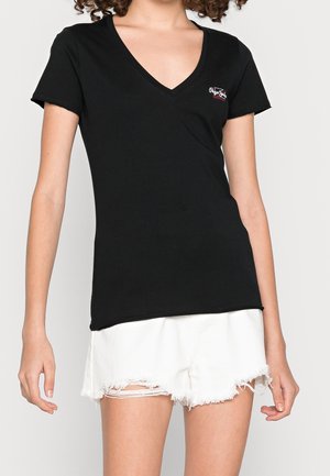 Czarny bawełniany t-shirt z dekoltem w serek, krótki rękaw i małe logo na lewej piersi. W zestawie z białymi szortami jeansowymi.