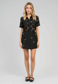 Chemisier noir en dentelle à manches courtes avec un design à boutons, associé à une jupe noire texturée arborant des broderies florales blanches et des accents métalliques.