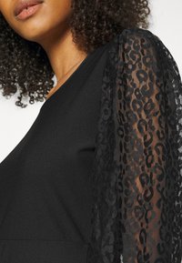 Vestido negro con un cuerpo sólido y mangas de encaje negro transparente con un patrón de leopardo. Textura suave con detalles en las mangas.