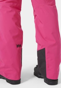 Jasně růžové voděodolné kalhoty s černými prvky, které mají hladkou texturu, přímý střih a detail loga na boku.