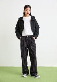 Sort cropped jakke med hætte, sammen med høj talje sorte pinstripe-bukser og sorte sneakers. Hvid t-shirt under.