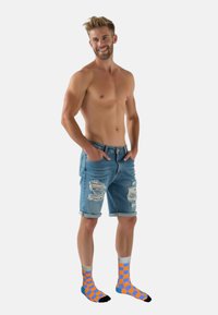 Lysblå denimshorts med slidser, parret med lyseorange og blå ternede sokker. Har en afslappet pasform og opsmældte bredder.
