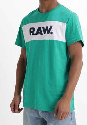 Green cotton T-shirt with a white horizontal stripe featuring "RAW." in navy blue. Short sleeves, crew neckline, relaxed fit.
