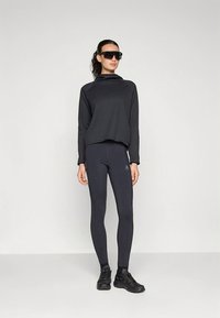 Fekete bordázott, rövid felső, fekete testhezálló leggingszel párosítva. A modell sötét napszemüveget és fekete sportcipőt visel.