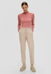 Lange mouw, geribbeld roze top gecombineerd met beige, verstelbare cargobroek met zijzakken en tan enkelboots met een dikke zool.