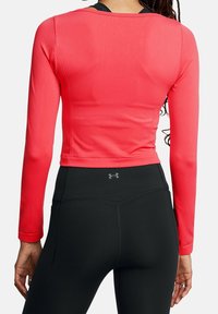 Červený atletický top s dlouhým rukávem a přiléhavým střihem, kombinovaný s černými legínami s vysokým pasem. Hladká textura bez viditelných vzorů či kovových doplňků.