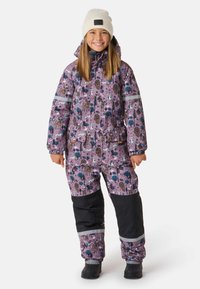 Paarse geïsoleerde skipak met dieren- en bomenpatronen, zwarte accenten bij de onderbenen en een reflecterende band. Katoenen muts op het hoofd gedragen.