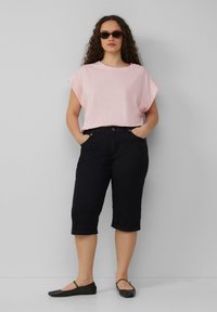 Haut rose clair à manches courtes associé à un pantalon capri noir. La tenue présente une coupe décontractée et des chaussures noires plates.