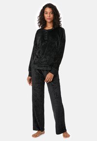 Conjunto de pijama de velour negro que incluye una blusa de manga larga con cierre de botones y pantalones holgados con un acabado texturizado y estampado.